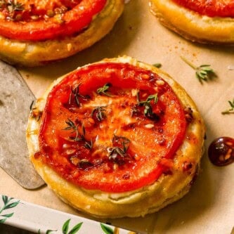Three tomato puff pastry tarts on a parchment-lined serving platter with a silver serving spatula.