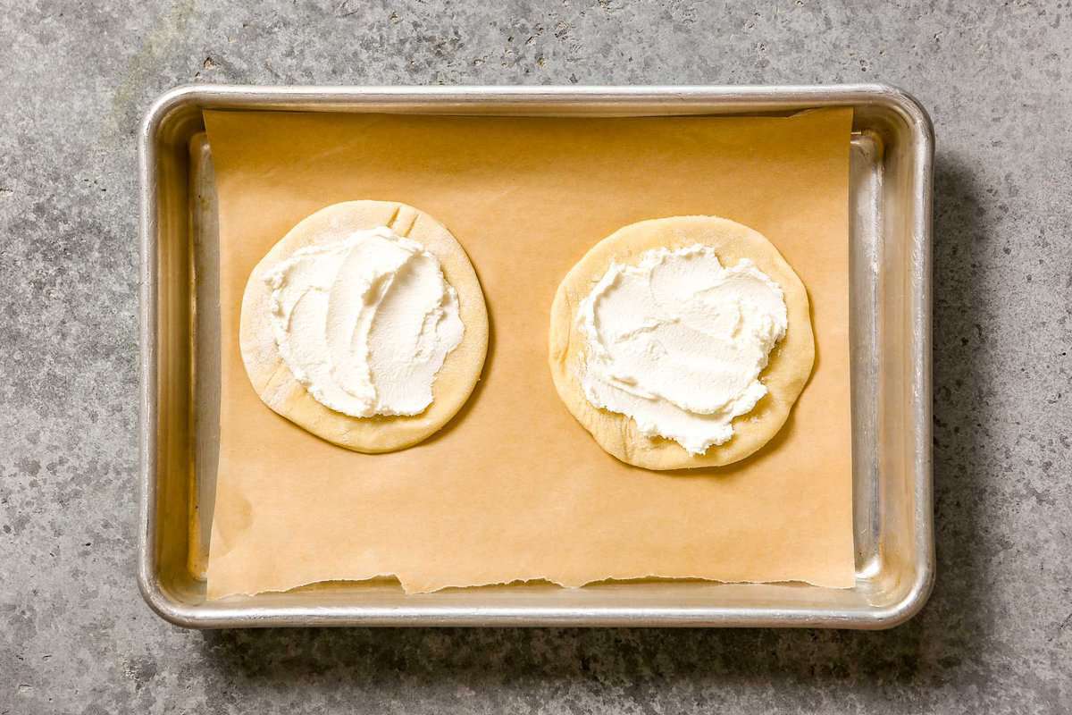 Two puff pastry rounds topped with goat cheese on a parchment-lined baking sheet.