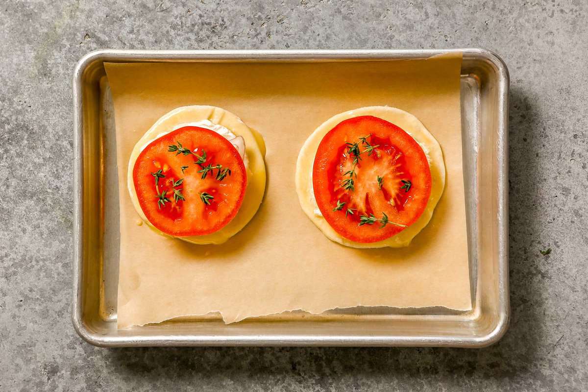 Two puff pastry rounds topped with goat cheese, tomato slice and thyme on a parchment-lined baking sheet.