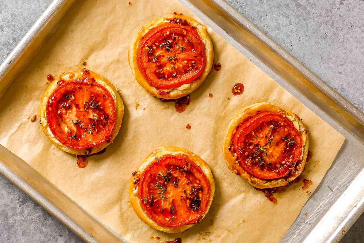 Four tomato puff pastry tarts on a parchment-lined baking sheet.