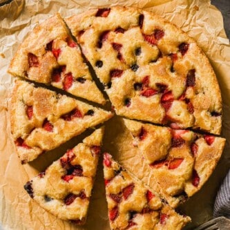 Berry cake cut into wedges on a piece of parchment paper.