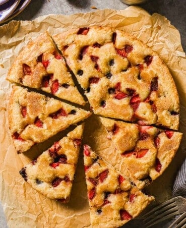 Berry cake cut into wedges on a piece of parchment paper.