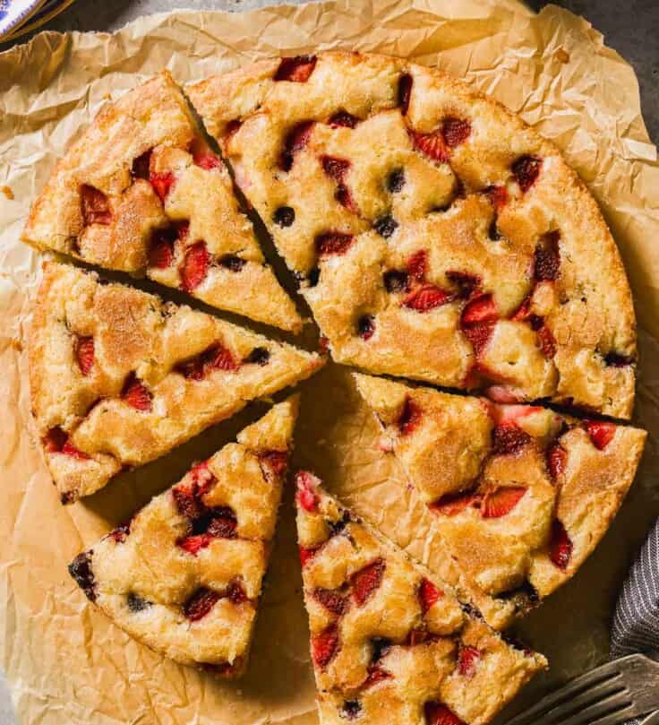 Berry cake cut into wedges on a piece of parchment paper.