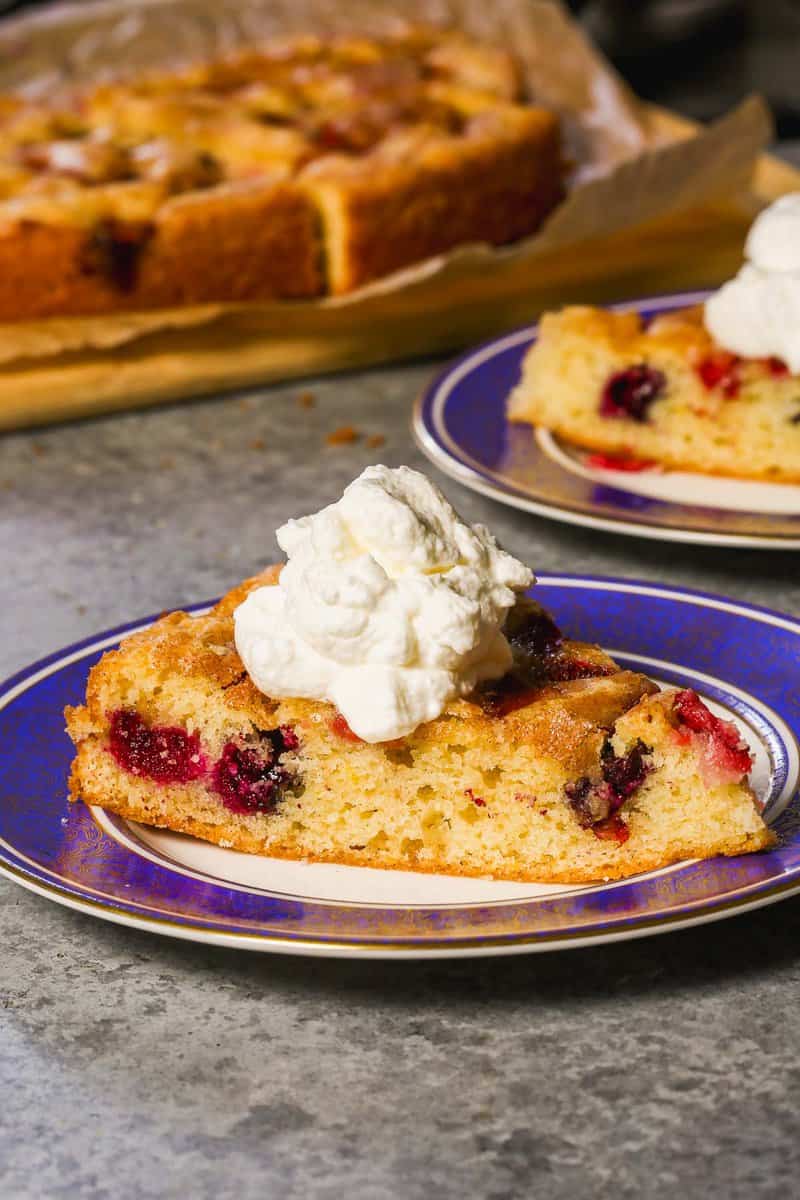 Slice of berry cake on a plate topped with a dollop of whipped cream.