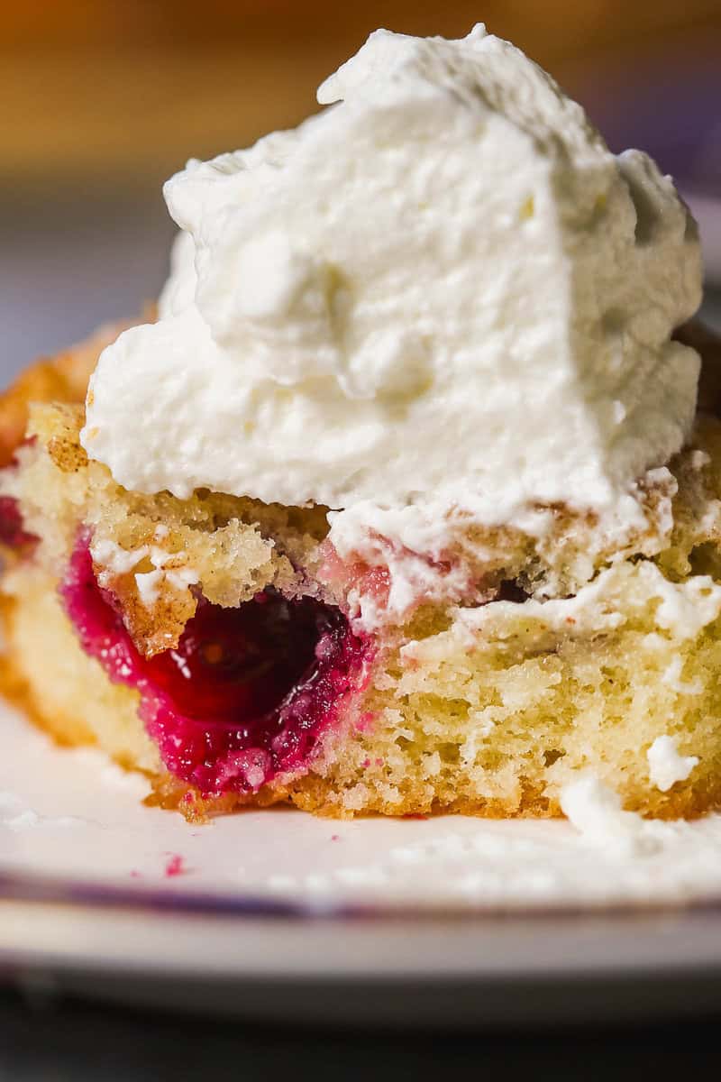 Slice of berry cake on a plate topped with a dollop of whipped cream.