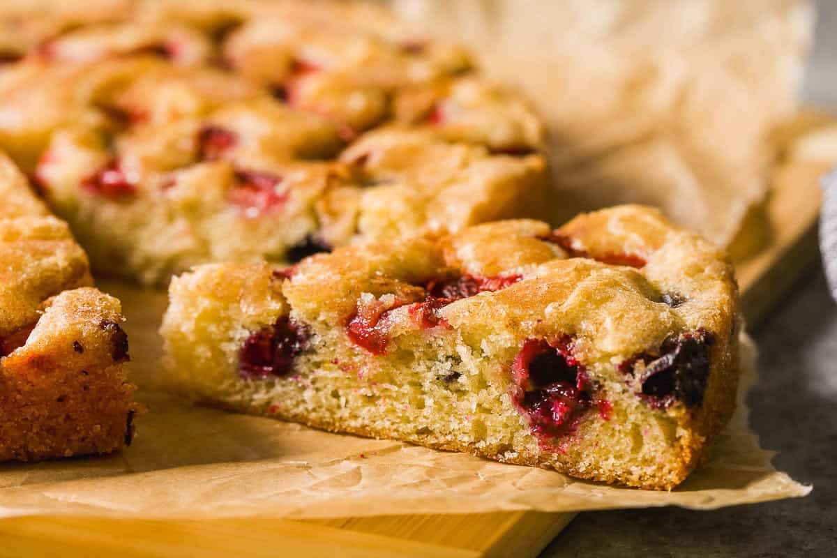 Slice of berry cake on a parchment-lined wood cutting board.