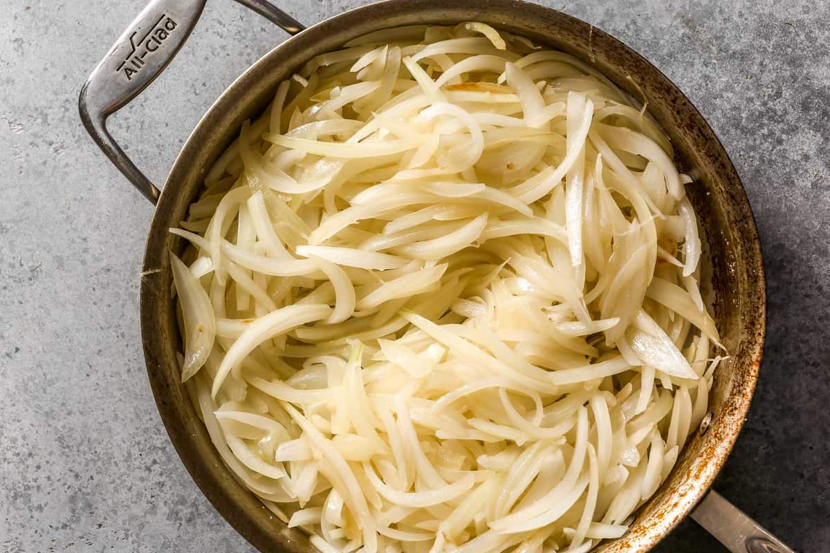 Sliced onions piled high into a sauté pan.