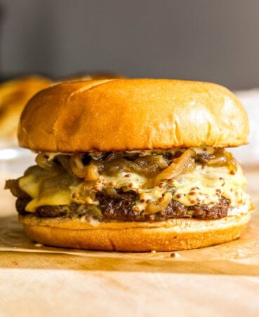 Smash burger topped with caramelized onions, cheese and sauce set on a piece of brown parchment paper on a wood cutting board.