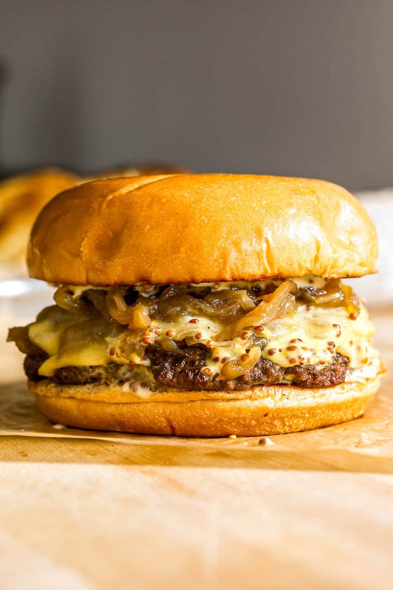 Smash burger topped with caramelized onions, cheese and sauce set on a piece of brown parchment paper on a wood cutting board.