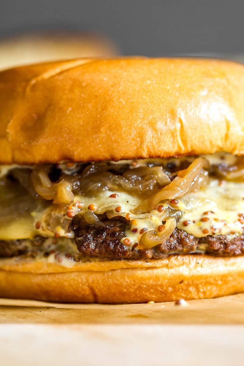 Caramelized onion burger set on a piece of brown parchment paper on a wood cutting board.