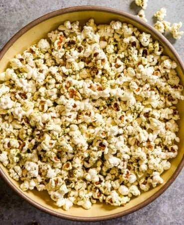 Herby popcorn in a large yellow bowl with kernels scattered around.