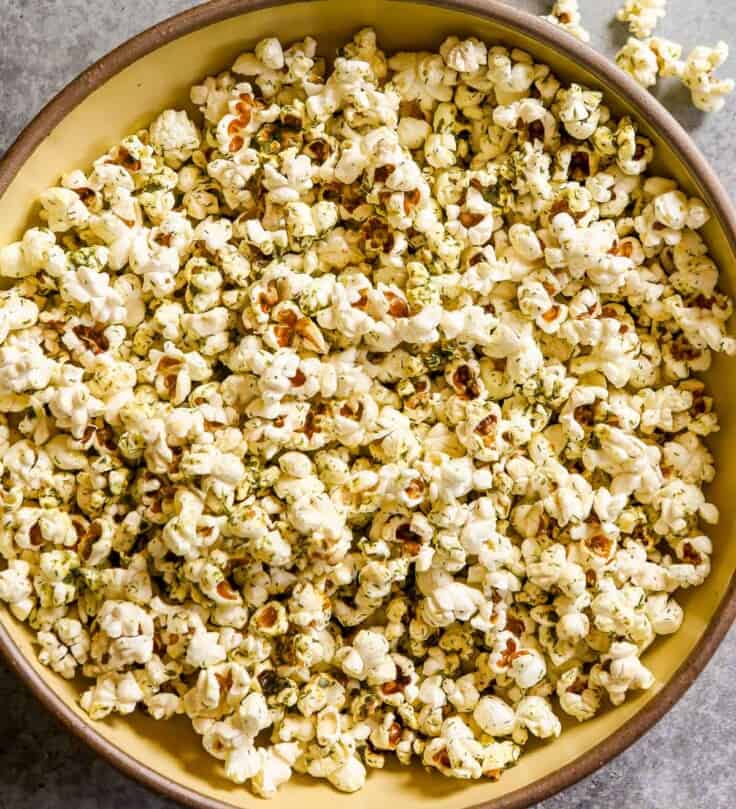 Herby popcorn in a large yellow bowl with kernels scattered around.