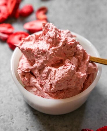 Strawberry flavored whipped cream in a small white bowl with a small wooden spoon set in it.