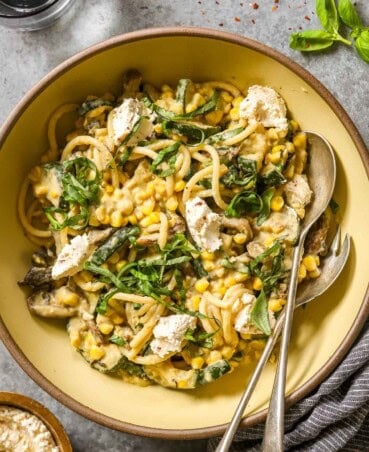 Creamy mushroom zucchini pasta in a yellow bowl with corn and dollops of ricotta and fresh basil.