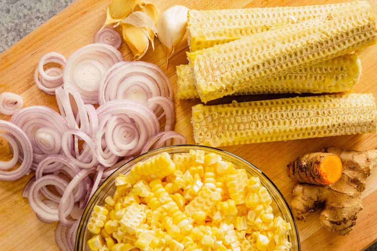 corn cobs, sliced shallots, garlic and turmeric on a wood cutting board