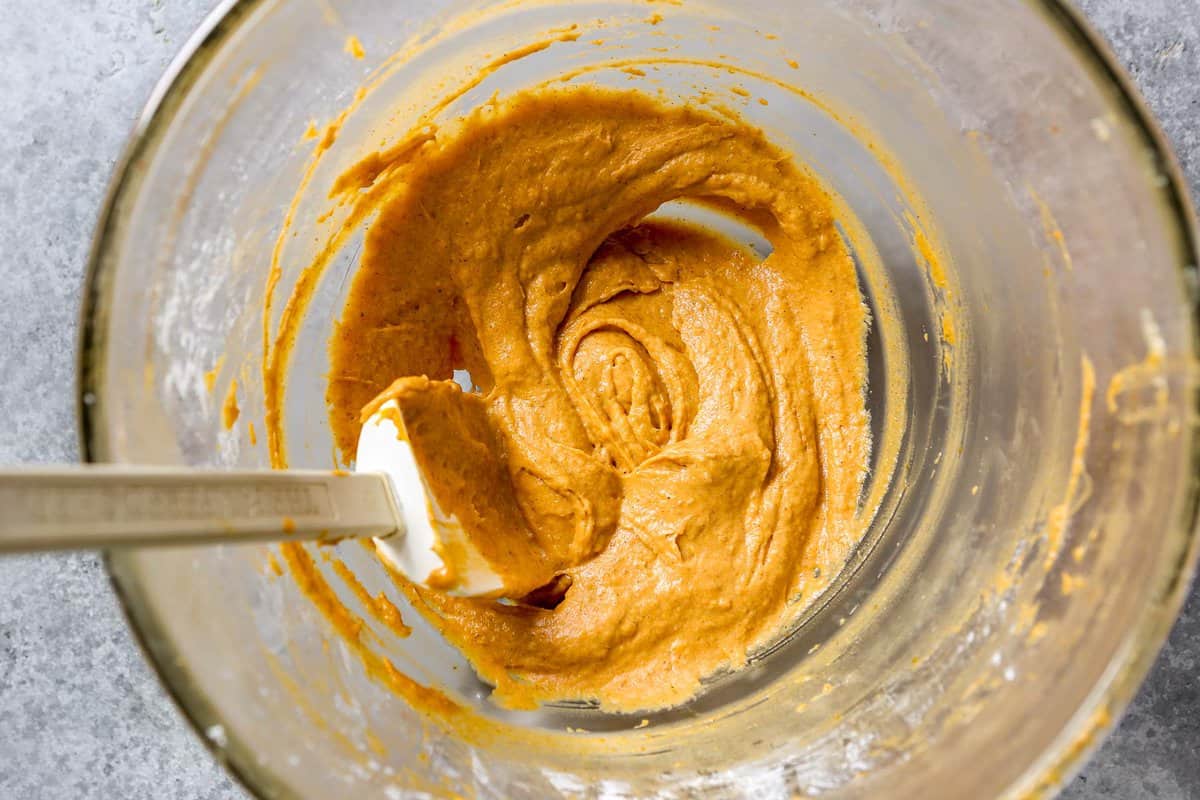 Pumpkin pie cookie filling in a glass mixing bowl with a white rubber spatula set in it.