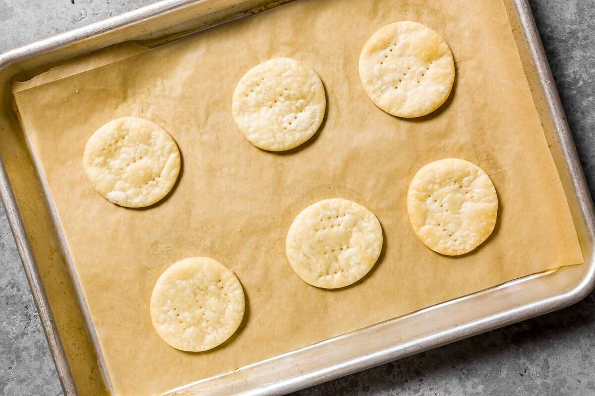 Six baked mini pie crust rounds on a parchment-lined baking sheet.