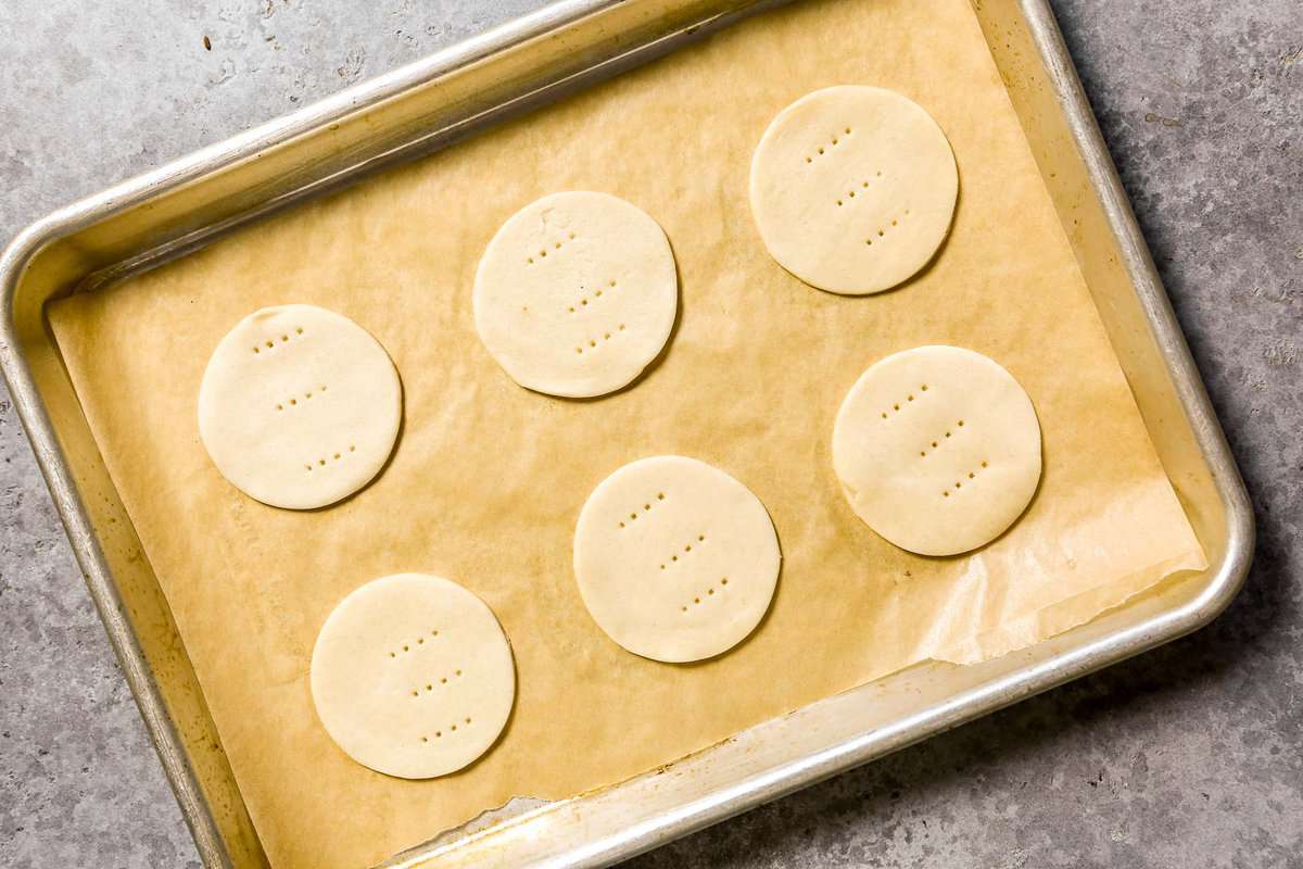 Six unbaked mini pie crust rounds on a parchment-lined baking sheet.