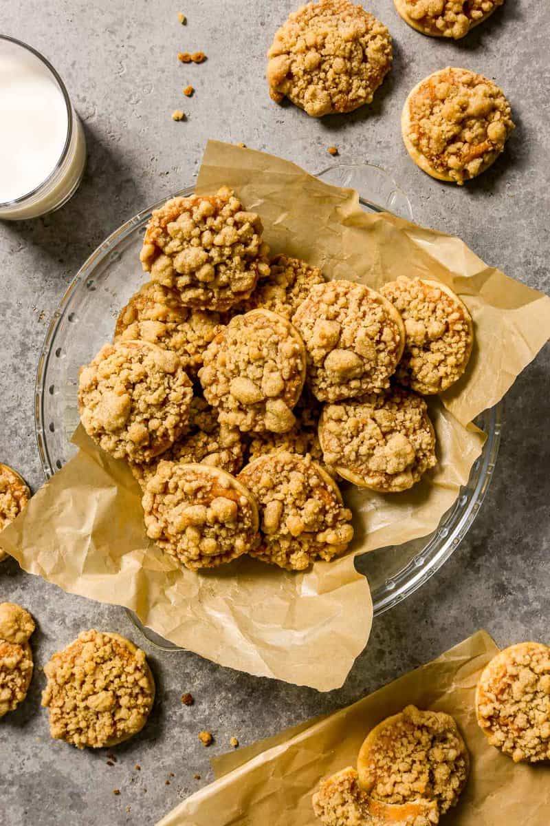 Pumpkin pie cookies, with a streusel topping, piled into a parchment-lined pie plate with cookies and milk set around it.