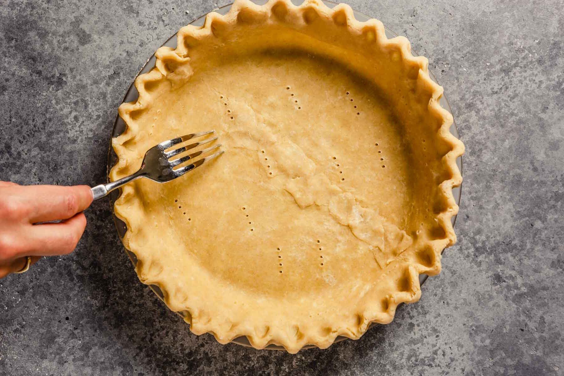 A fork pricking an unbaked pie crust.