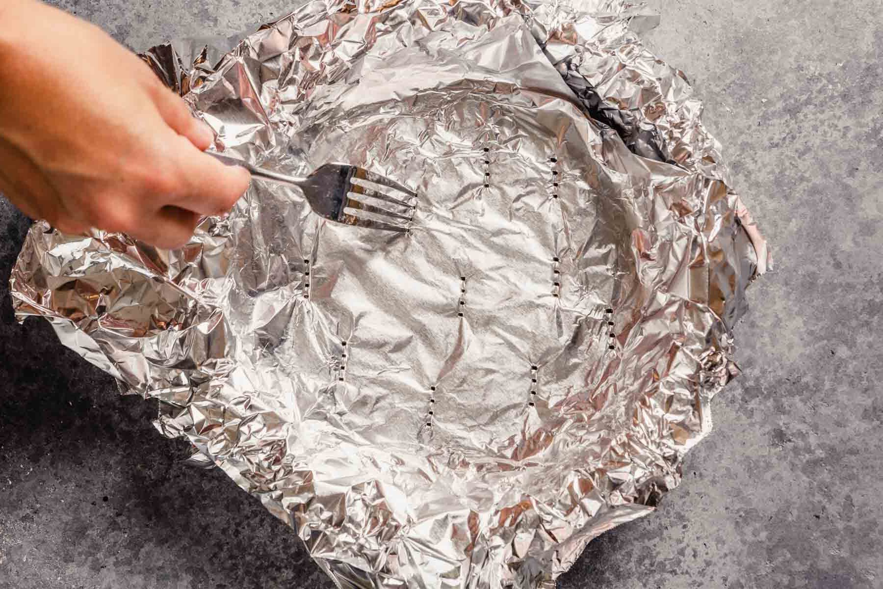 A fork pricking a layer of foiling lining a pie plate. 