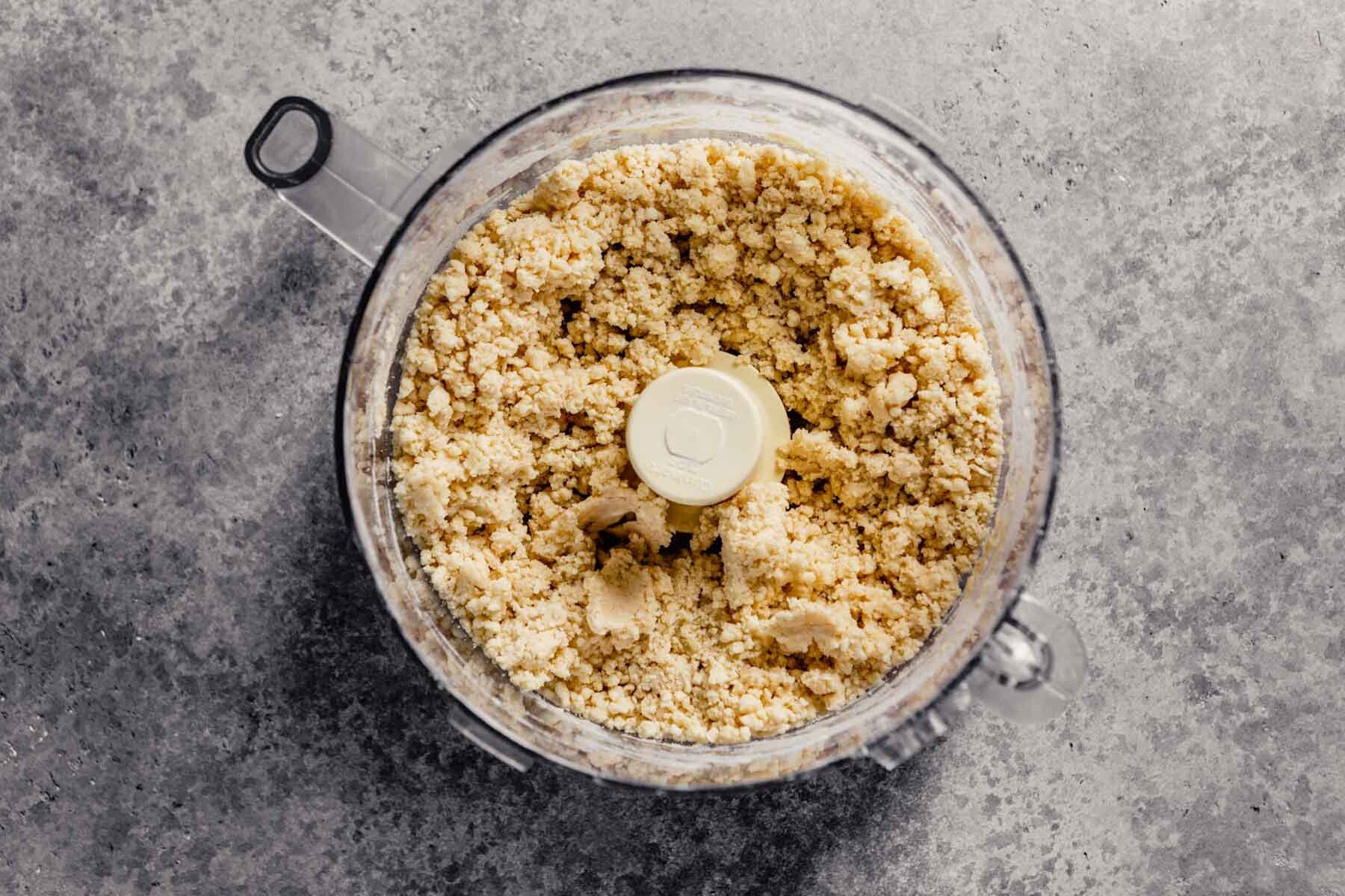 crumbly pie crust dough in a food processor on a counter. 