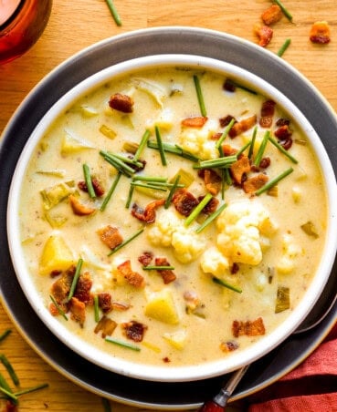 Creamy cauliflower potato leek soup in a shallow white bowl topped with bacon bits and chives.