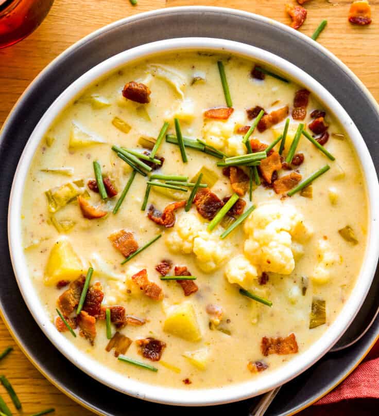 Creamy cauliflower potato leek soup in a shallow white bowl topped with bacon bits and chives.