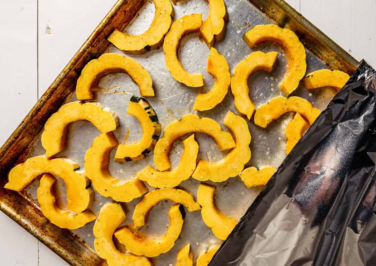 Half moon slices of delicata squash on a baking sheet partially covered with foil.