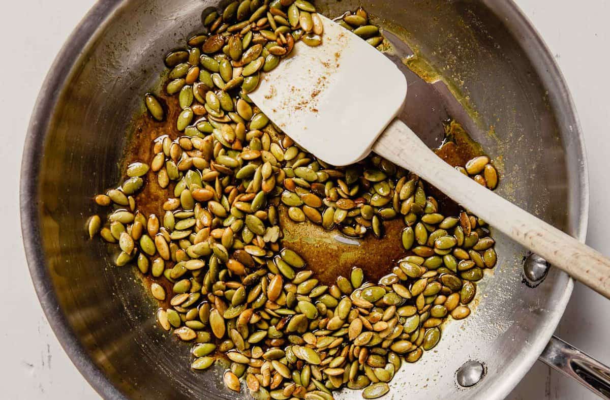 Pepitas cooking in browned butter in a skillet with a white rubber spatula.