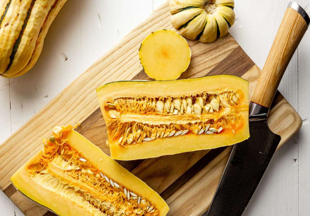 Delicata squash cut in half on a wood cutting board. 