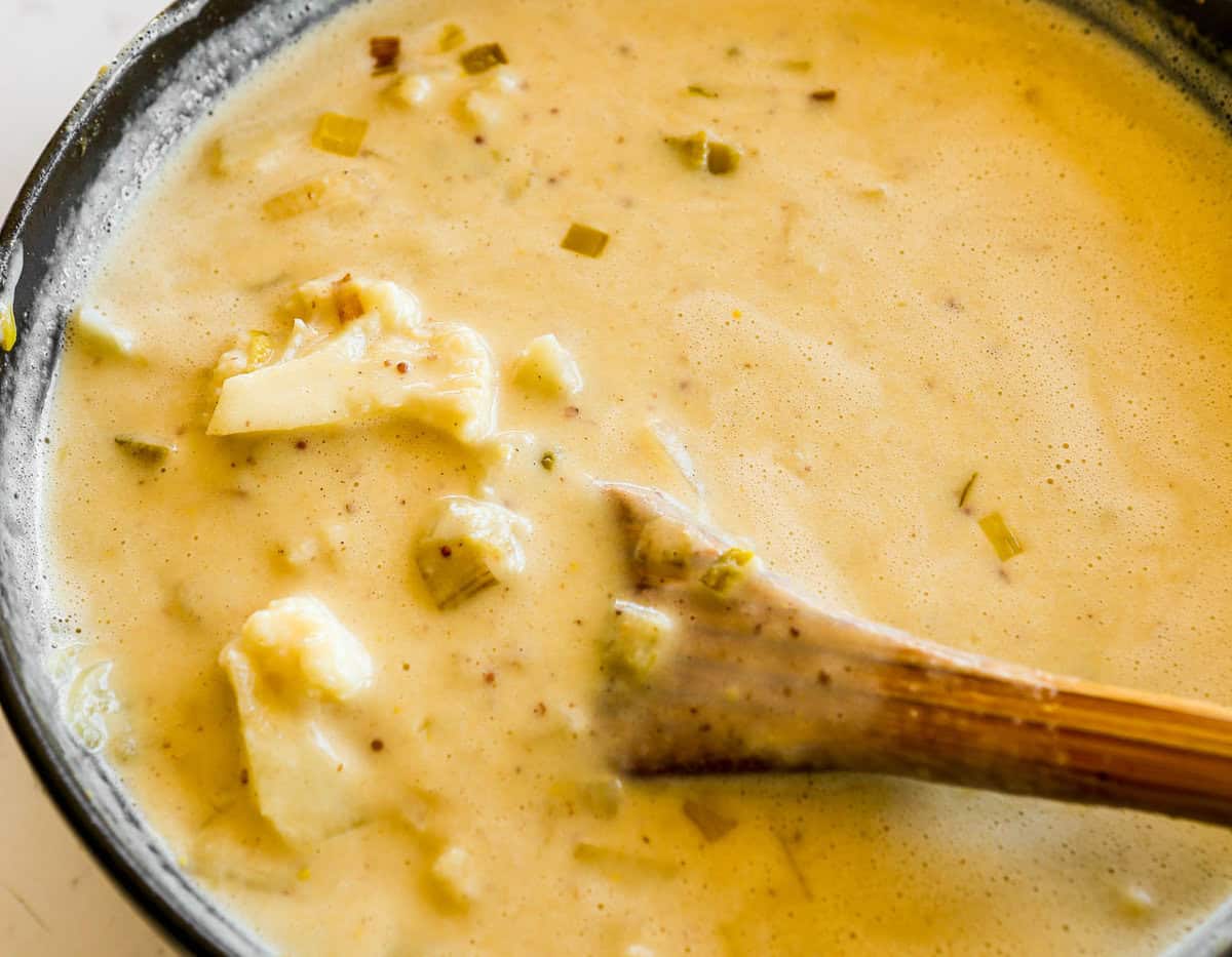 Creamy soup in a pot, wooden spoon stirring and scooping up a piece of cauliflower.