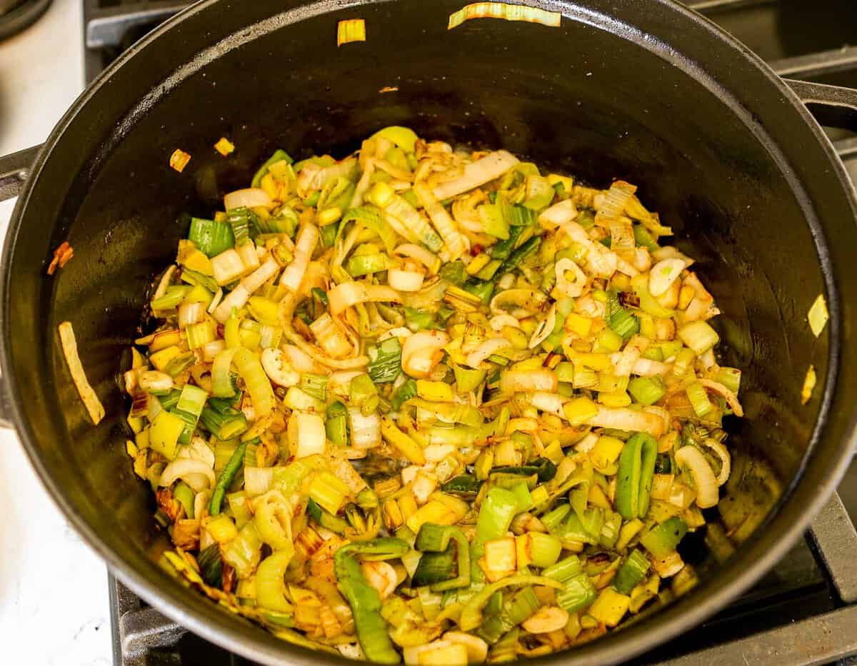 Sliced leeks and garlic cooking in a black dutch oven.