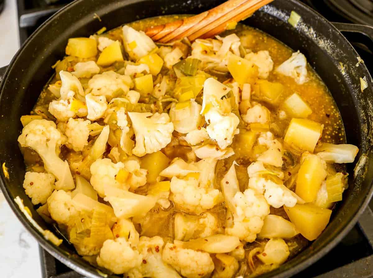 Chunks of potatoes and cauliflower cooking in broth in a large pot.