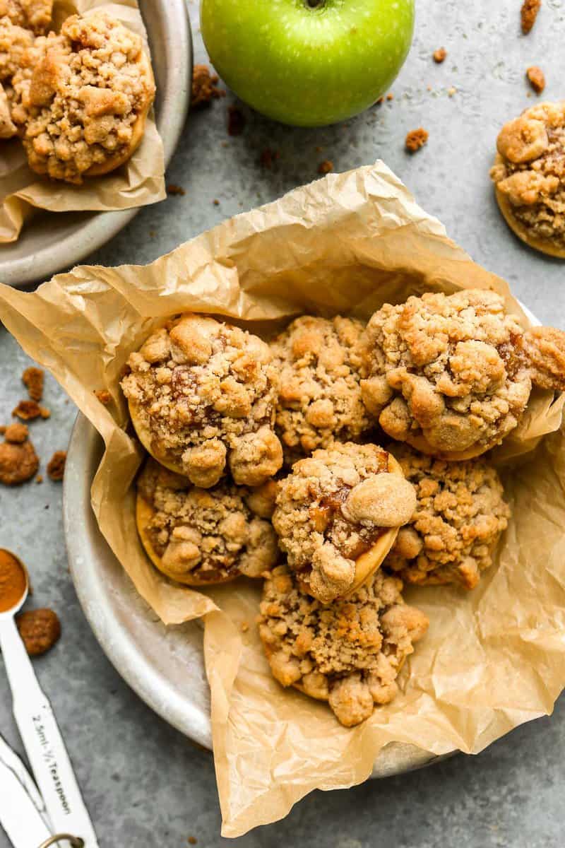 Apple pie cookies (pie crust rounds topped with apple pie filling and topped with streusel) arranged in a parchment-lined pie plate.