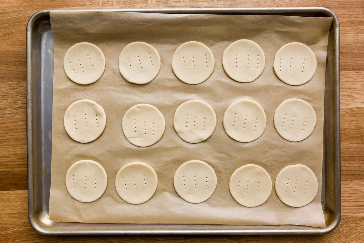 Unbaked pie crust rounds, each pricked with a fork three times, set on a parchment-lined baking sheet.