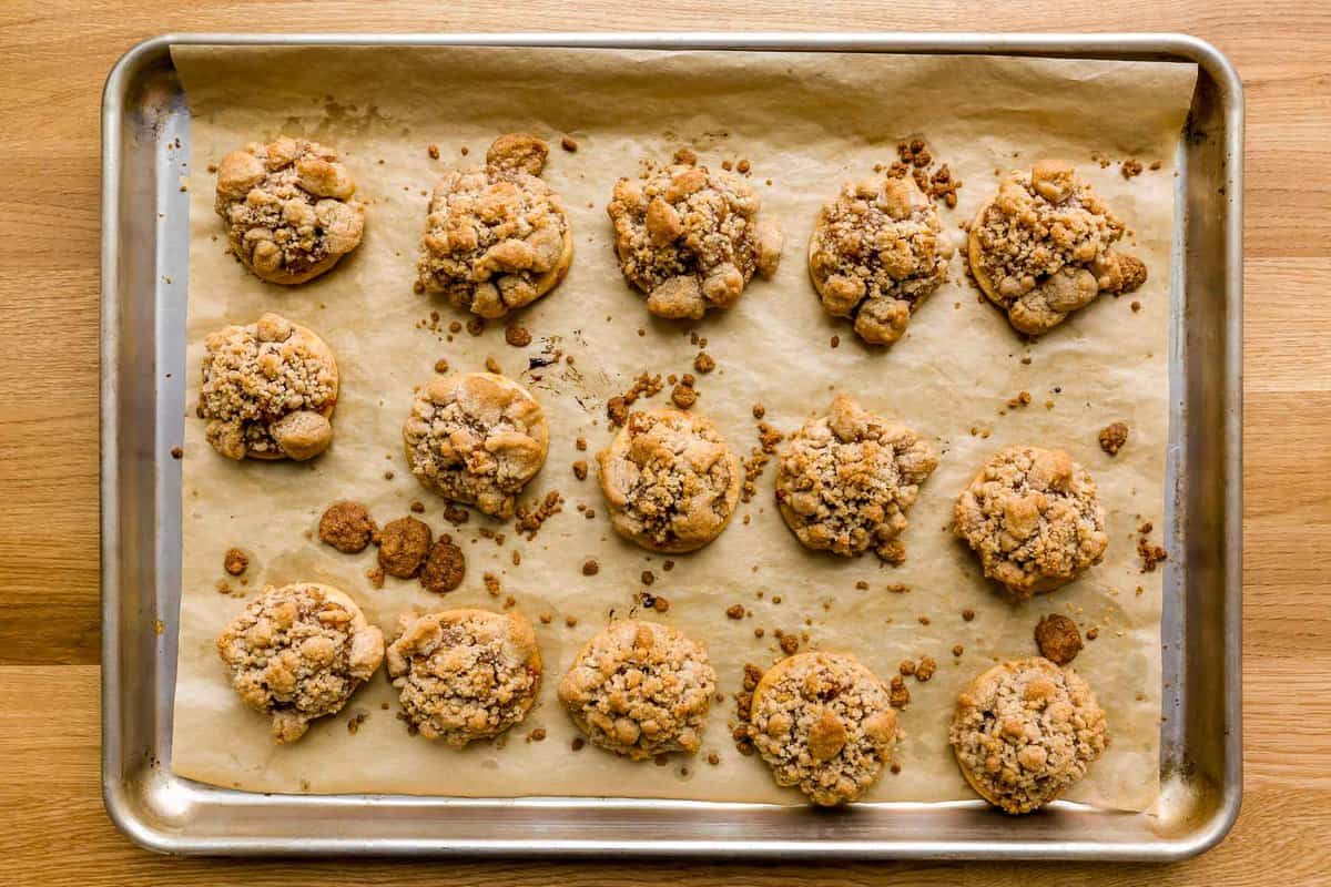 Baked apple pie cookies set on a parchment-lined baking sheet with baked bits of streusel on the sheet pan.