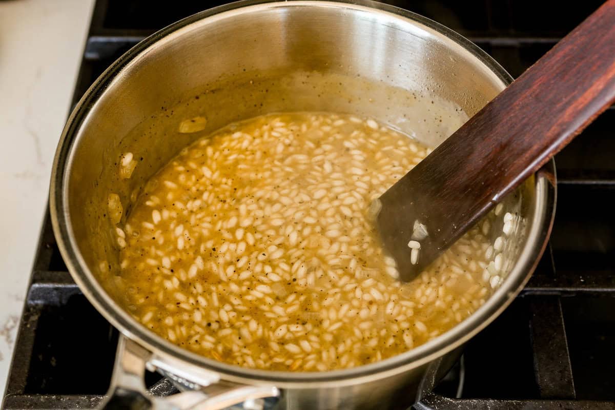 Risotto cooking in saucepan with a wooden spoon set in it.