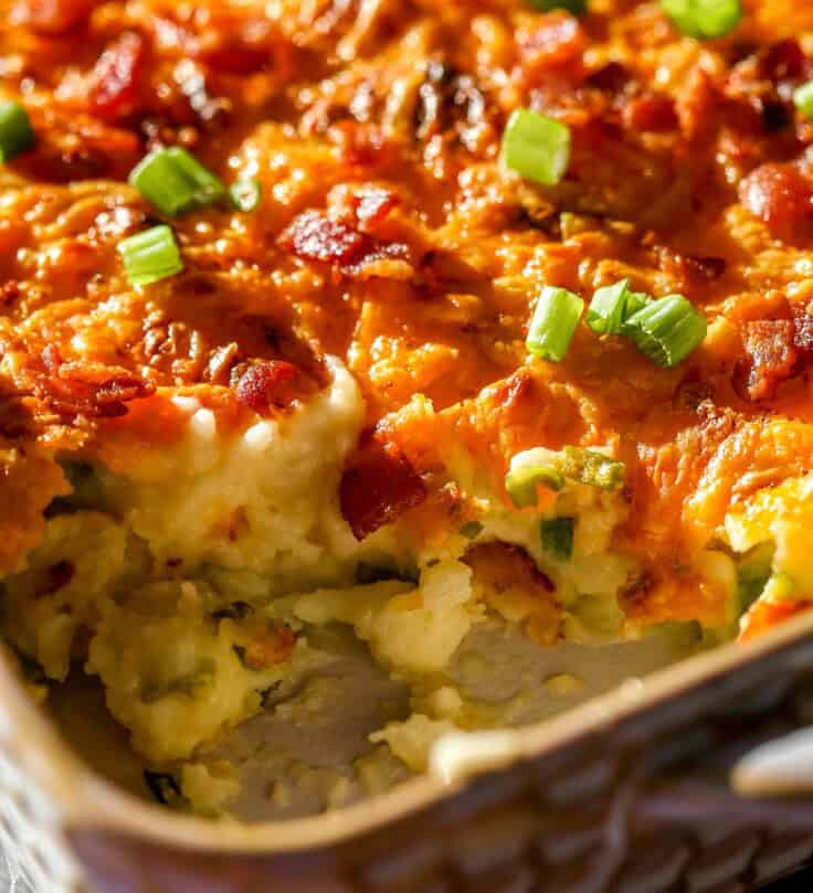 Baked mashed potatoes in a baking dish topped with melted and golden brown cheese, chopped scallions and bacon bits.