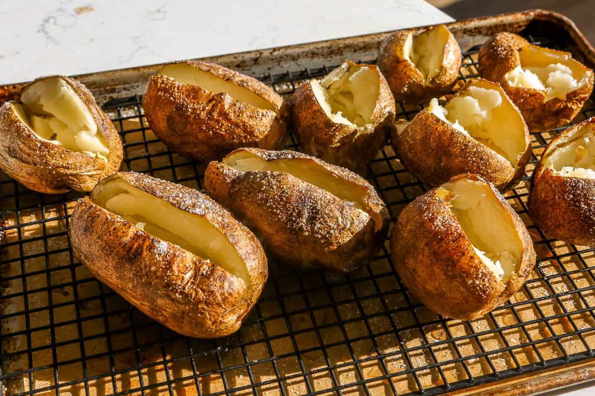 Baked potatoes baked and split open on a baking sheet lined with parchment paper and a black wire rack.