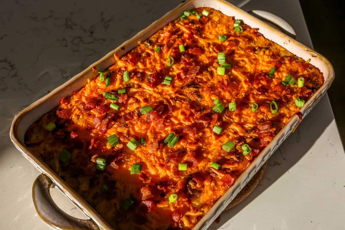 Baked mashed potatoes in a baking dish topped with melted and golden brown cheese, chopped scallions and bacon bits.