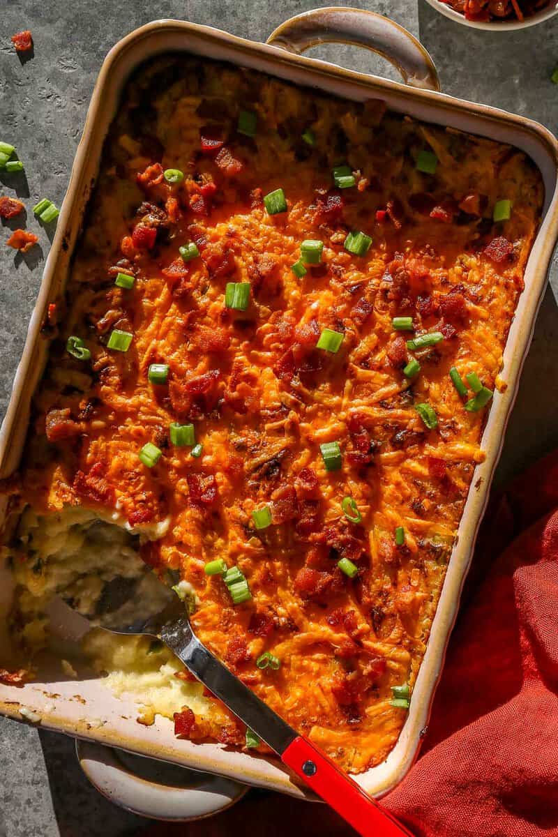 Baked mashed potatoes in a baking dish topped with melted and golden brown cheese, chopped scallions and bacon bits.