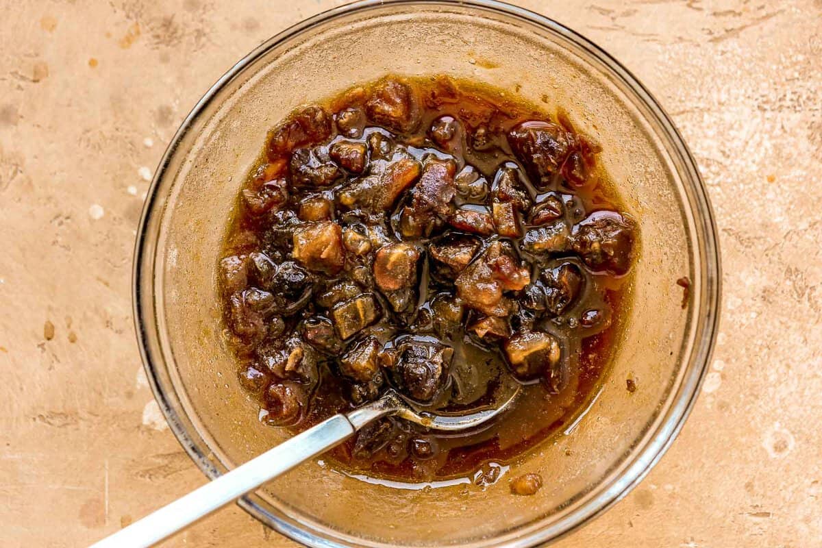 Chopped dates and root beer in a glass bowl with spoon.