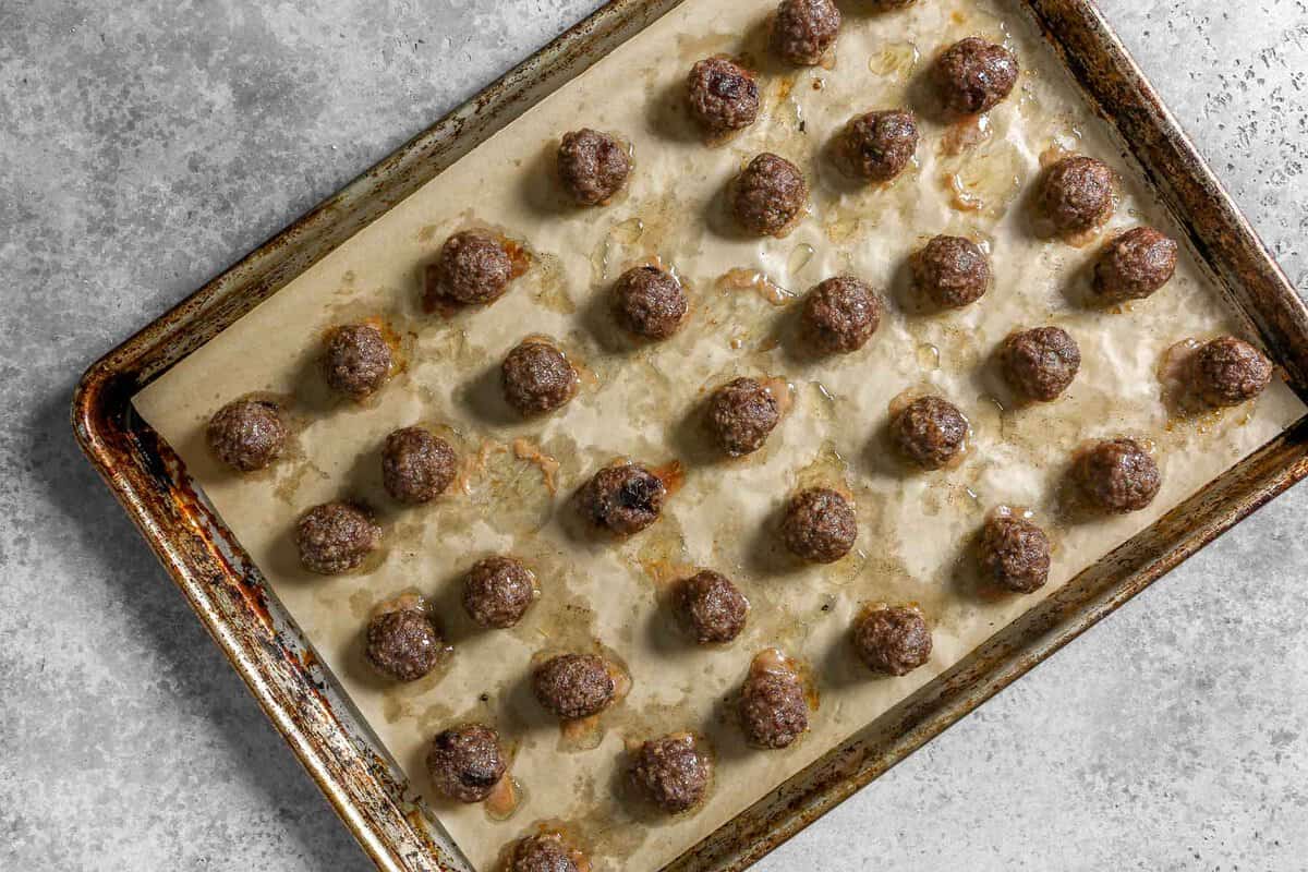 Parchment lined baking sheet with baked meatballs set on it arranged in even rows.