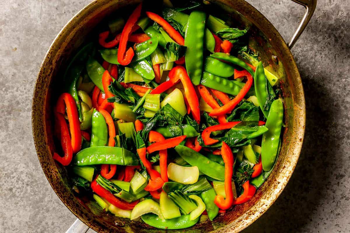 Cooked strips of red bell pepper, chunks of bok choy and snow peas in a large saute pan.