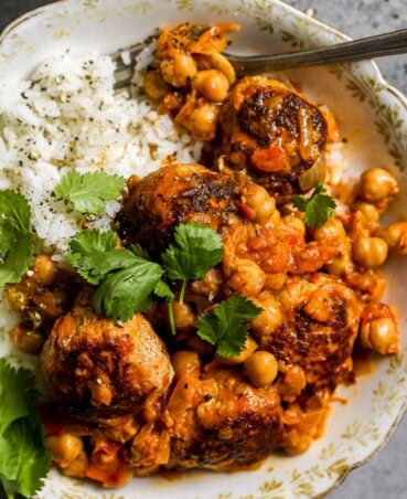 Gold and white bowl filled with rice and topped with meatballs and chickpeas coated in a creamy harissa sauce. Topped with a few cilantro leaves.