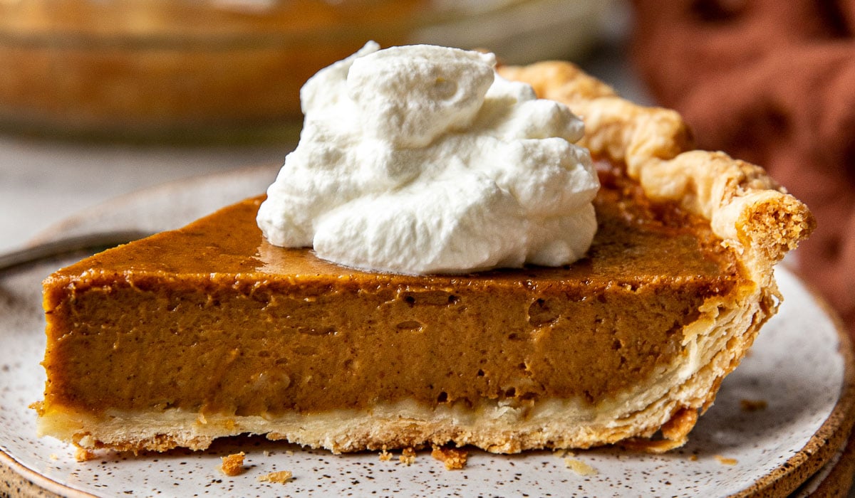 Slice of pumpkin pie on a speckled plate, showing the creamy filling and the flaky all butter pie crust.
