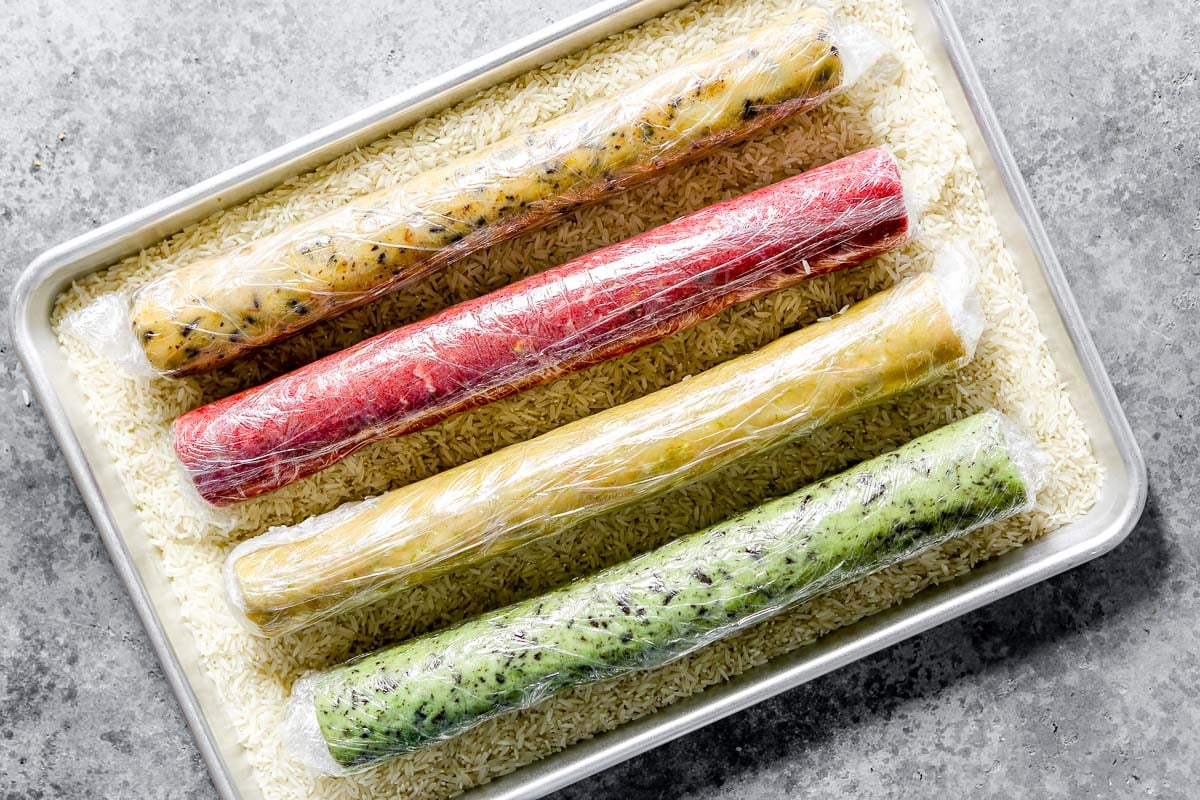 Colorful logs of cookie dough set in a baking sheet filled with rice.