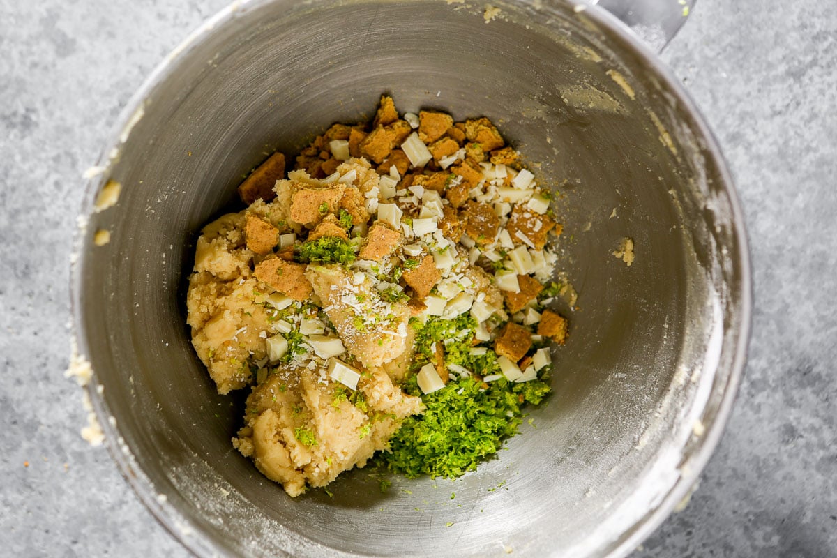 Cookie dough in a metal mixing bowl topped with graham crackers, white chocolate and lime zest.