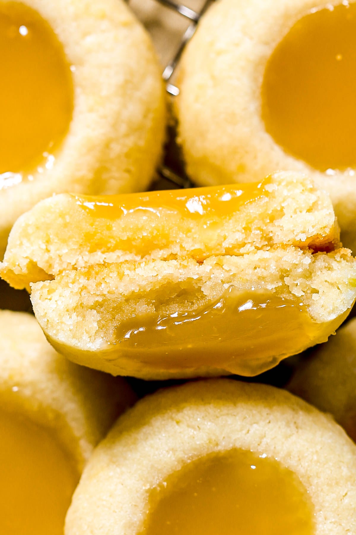 Lemon thumbprint cookie, broken in half to show the buttery cookie and jammy lemon curd, set on top of more thumbprint cookies.